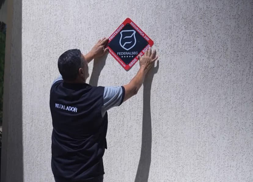 Instalador fixando a placa Protegido Federal Seg na fachada